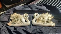 Top view of the pair of plaster swan wall plaques showing gold, white, and ivory painted detail and sculpted wings.