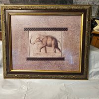 Framed print of an elephant in an ornate gold-tone frame with textured beige mat and glass covering.