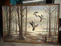 Full view of the framed painting showing a winter forest scene with three ducks flying.