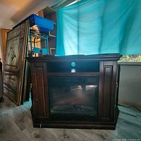 Front and side views of the electric fireplace unit showing deep wood finish, central firebox with realistic log display, open shelf above it with cable management hole, and side glass-panel doors with interior shelves.