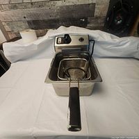 Full view of the stainless steel deep fryer with basket featuring black insulated handle showing wear and a smaller mesh basket inside.