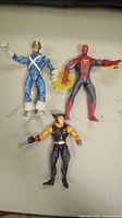 Three Marvel Legends action figures including Cyclops, Spider-Man, and Wolverine arranged on flat surface.