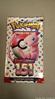 Front view of the sealed Pokémon Scarlet & Violet 151 booster pack featuring Mew and a Poké Ball with colorful silhouettes in the background.