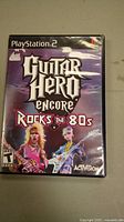 Front cover of the PlayStation 2 game case for Guitar Hero Encore Rocks the 80s with characters and logo.
