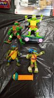 All four Teenage Mutant Ninja Turtles figures displayed together with the PEZ dispenser on a black surface.