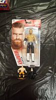 Photo of sealed Buddy Murphy WWE wrestling figure with two small status figures on a black surface.