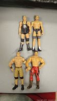 Four WWE wrestler action figures in different outfits laid out on a grey surface, showing full body and details.