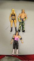 Three WWE wrestler action figures on flat surface, showing full body and attire details.