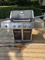 Front full view of Dyna-Glo gas BBQ showing four control knobs, side shelf, lower cabinet