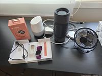 Overview showing Fitbit Versa 3 box and contents, Google Home, cylindrical speaker, desk fan, cables