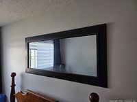 Front view of rectangular wood framed mirror mounted on wall