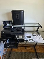 Printer and shredder on glass desk with manuals and cables