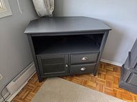 Front view of dark painted wood corner TV cabinet showing open shelf, mesh door and two drawers
