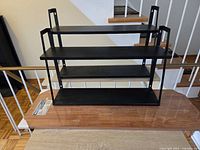 Black three-tier wall shelf, wood boards in background