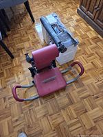 Merach pedal bike still boxed beside red AB Rocket Twister chair