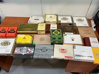 Top-down view of 22 empty cigar boxes arranged on two tables, clearly showing box branding and condition.