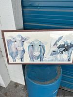 Photo of the full artwork showing three cows with pastel blue and purple tones, framed in wood.
