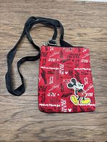Front angled view of red Mickey Mouse fabric purse with black adjustable strap on wood surface