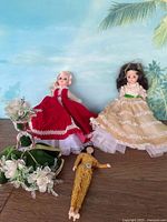 Three assorted dolls including one in beige dress with green belt, one in red dress with lace, and one smaller doll in leopard print bodysuit.
