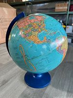 Front side of the globe showing North and South America with countries and major cities labeled. Globe mounted on blue plastic base with blue meridian.