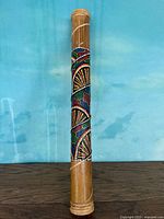 Full view of the wooden rain stick showing the cylindrical shape and hand painted colorful dot pattern wrapped around the middle portion.