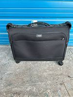 Front view of black Hartmann folding garment bag luggage showing zipper pocket and handle