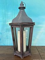 Front view of tall hexagonal wooden frame candle lantern with glass panels and metal top, white pillar candle inside.