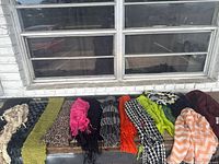 Wide angle photo showing multiple scarves unfolded and laid out for display, capturing variety of colors and textures.