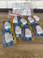 Lot overview of multiple white door and window alarms, some still in original packaging, others loose in plastic bags. Ample quantity for multiple installations.