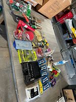Wide photo showing a lot of hardware and tools spread out on a table including drill bit sets, socket set, paint roller, wire brushes, and various small packets of screws and tools.
