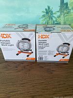 Pair of HDX portable halogen work lights in original boxes showing front side and product image with branding details.