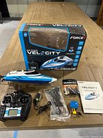 Box, RC boat, controller, batteries, charger, manual, and parts displayed on wooden table