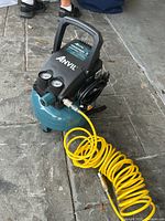 Front angle view highlighting the yellow coiled air hose, pressure gauges, and carry handle on blue tank compressor