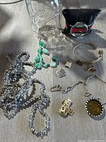Lot of assorted jewelry pieces including necklaces, pendants, bracelet, watch, displayed on surface with a clear Ball glass jar nearby.