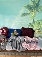 Overview of the sweatshirt lot showing various colors and designs, including Where's Waldo themed sweatshirt and hooded sweatshirts.