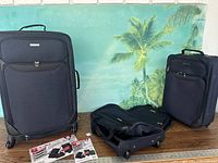 Photo showing the large suitcase with front zippered pocket, medium suitcase and a black rolling carry bag placed on table with a tropical background.