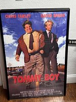 Full view of framed Tommy Boy movie poster showing Chris Farley and David Spade with text and some reflection on glass.