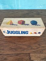 View of the full vintage juggling ball set box with cartoon-style illustrations of juggling props on the lid.