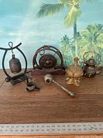 Overview of the lot including wooden gong and five metal decorative items on a wooden surface with leafy background.