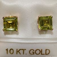 Close-up photo of the pair of 10K gold earrings set with square cut peridot stones on white display with 10 KT GOLD label visible.