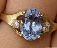 Front view on finger showing oval lavender-blue tanzanite and side diamonds set in yellow gold.