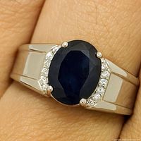 Close-up photo of the silver ring on finger showing the oval blue sapphire and small accent stones on the band.