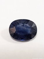 Front view of oval faceted dark blue enhanced sapphire gemstone.