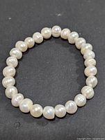 Close-up image of a white freshwater pearl flexible bracelet arranged in a circle on a black background, highlighting the individual pearls and their natural luster.