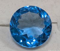 Close-up image of a single round cut blue topaz gemstone highlighting vivid blue color and facets.