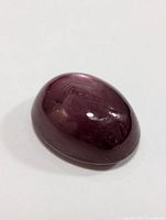 Oval cabochon cut star ruby showing reddish-purple color and star effect on polished surface.