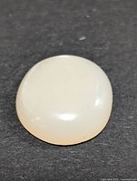 Clear close-up image of a smooth, dome-shaped white moonstone cabochon gemstone against a black background.