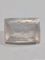Clear image of rectangular faceted pale pink rose quartz gemstone lying flat, showing brilliance and internal clarity.