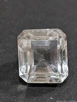 Top view of square emerald cut white topaz gemstone with stepped facets on a black background.