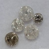Close up image of five natural diamonds with rough internal inclusions and varying brown to clear colors.